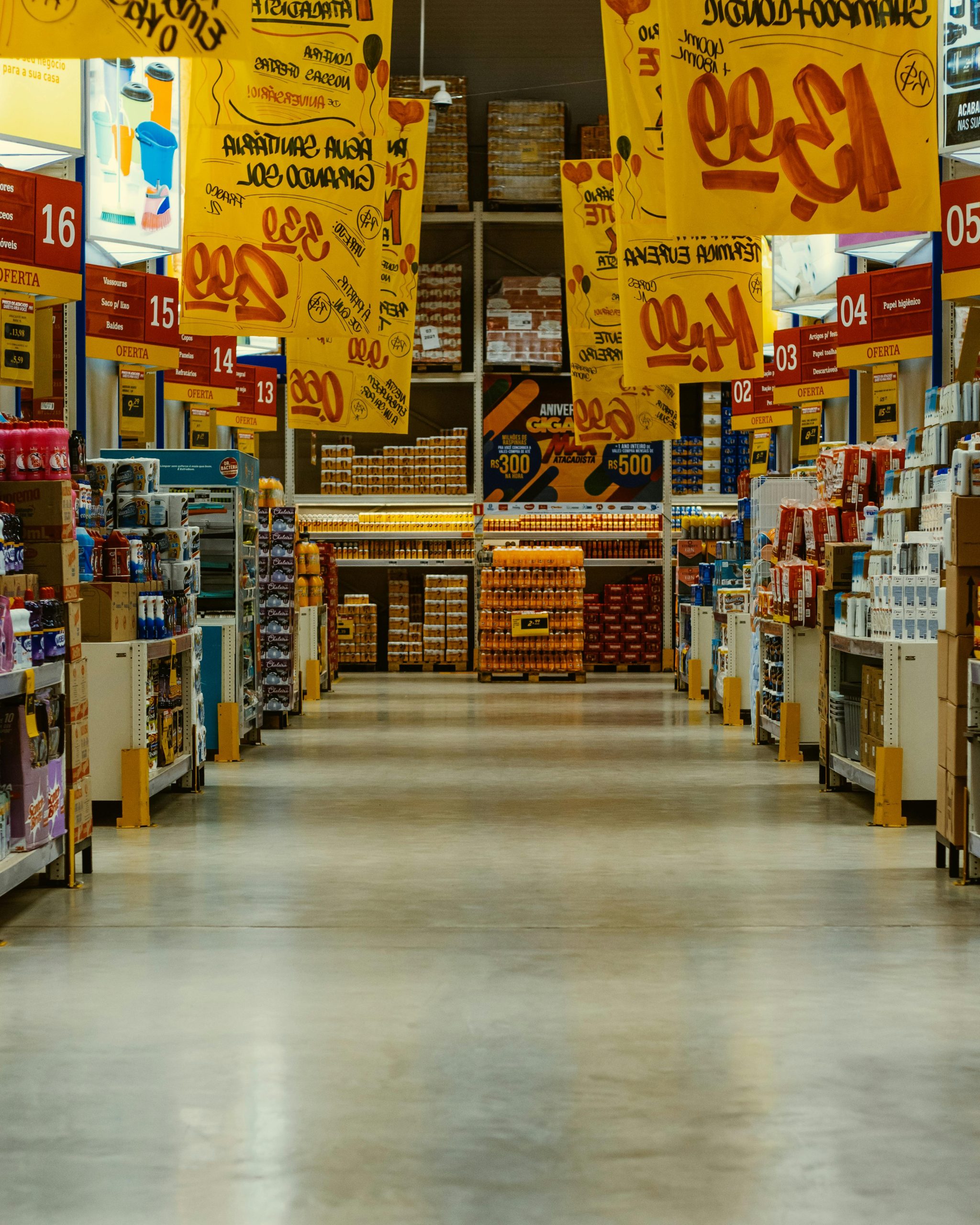 Home Wide supermarket aisle with colorful sale banners and stocked shelves in a vibrant Brazilian store.